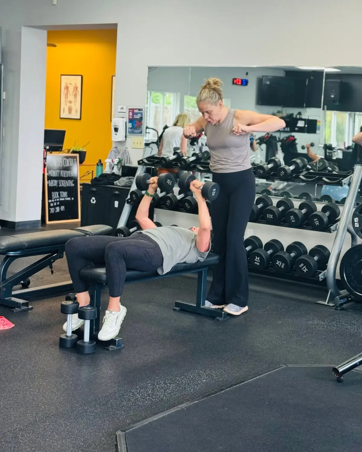 HealthSPORT personal trainer spotting a member through a heavy dumbbell bench press