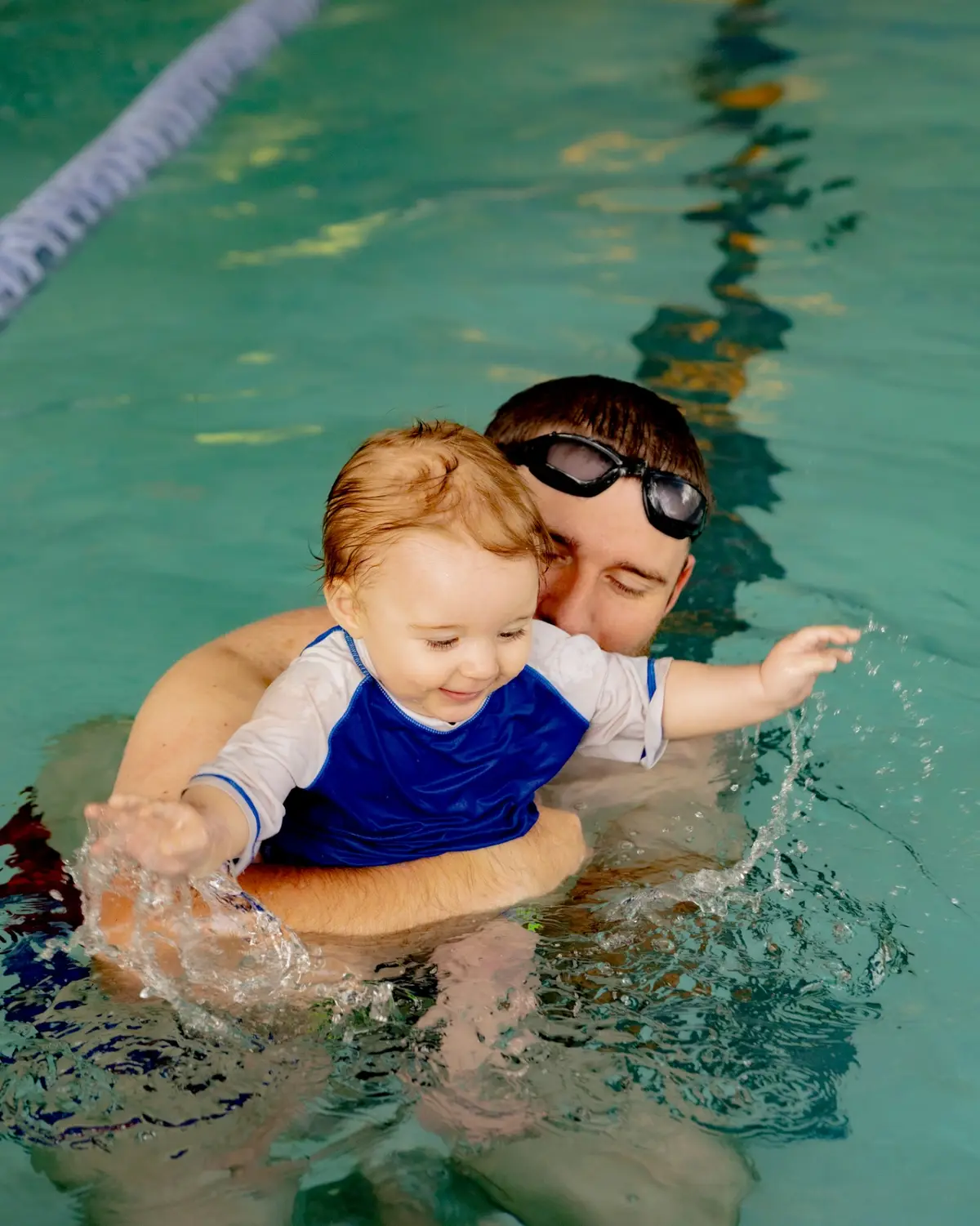 Toddler splashing with dad in the heated indoor pool
