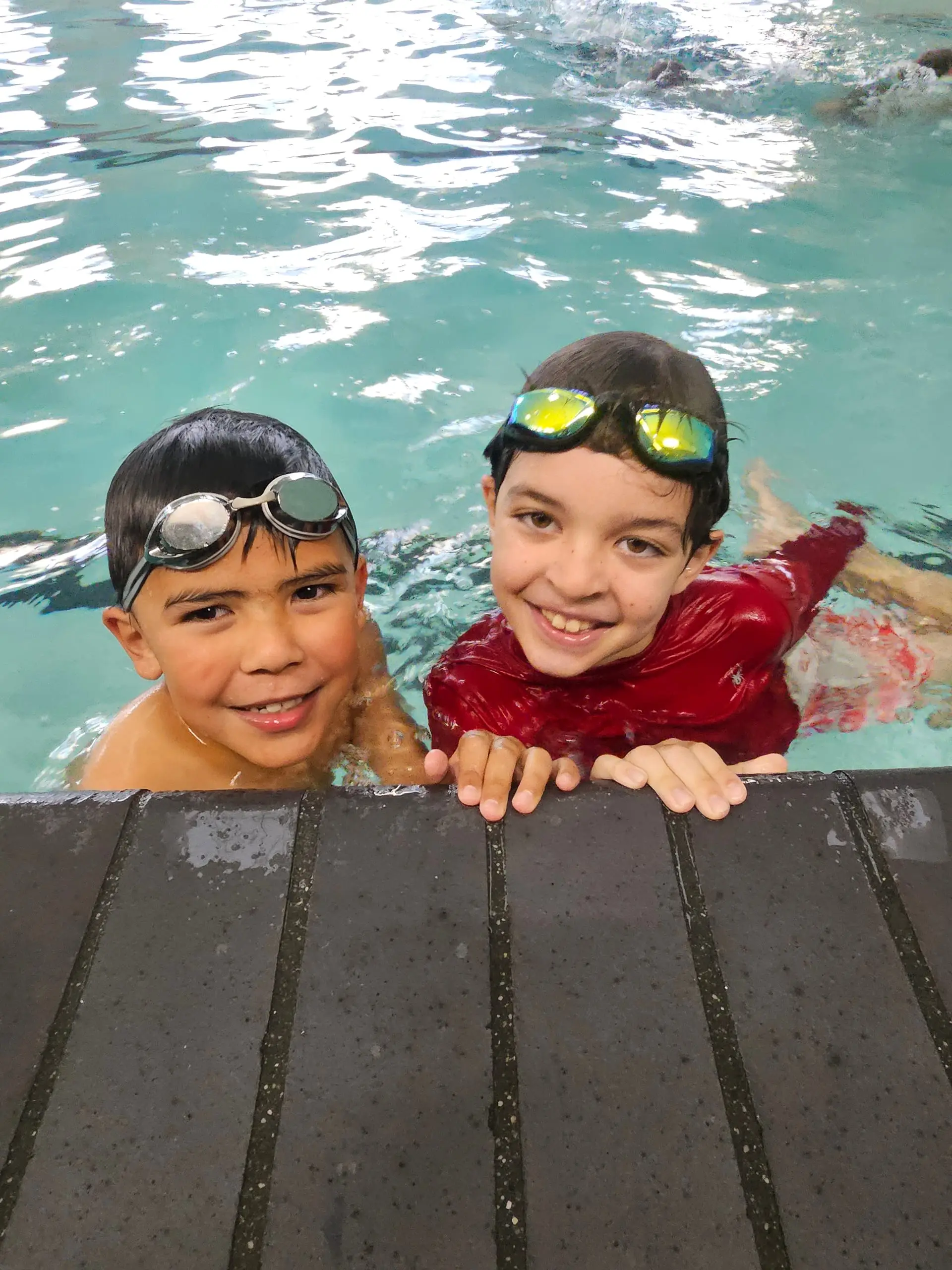 Two swim school students in goggles at the pool wall