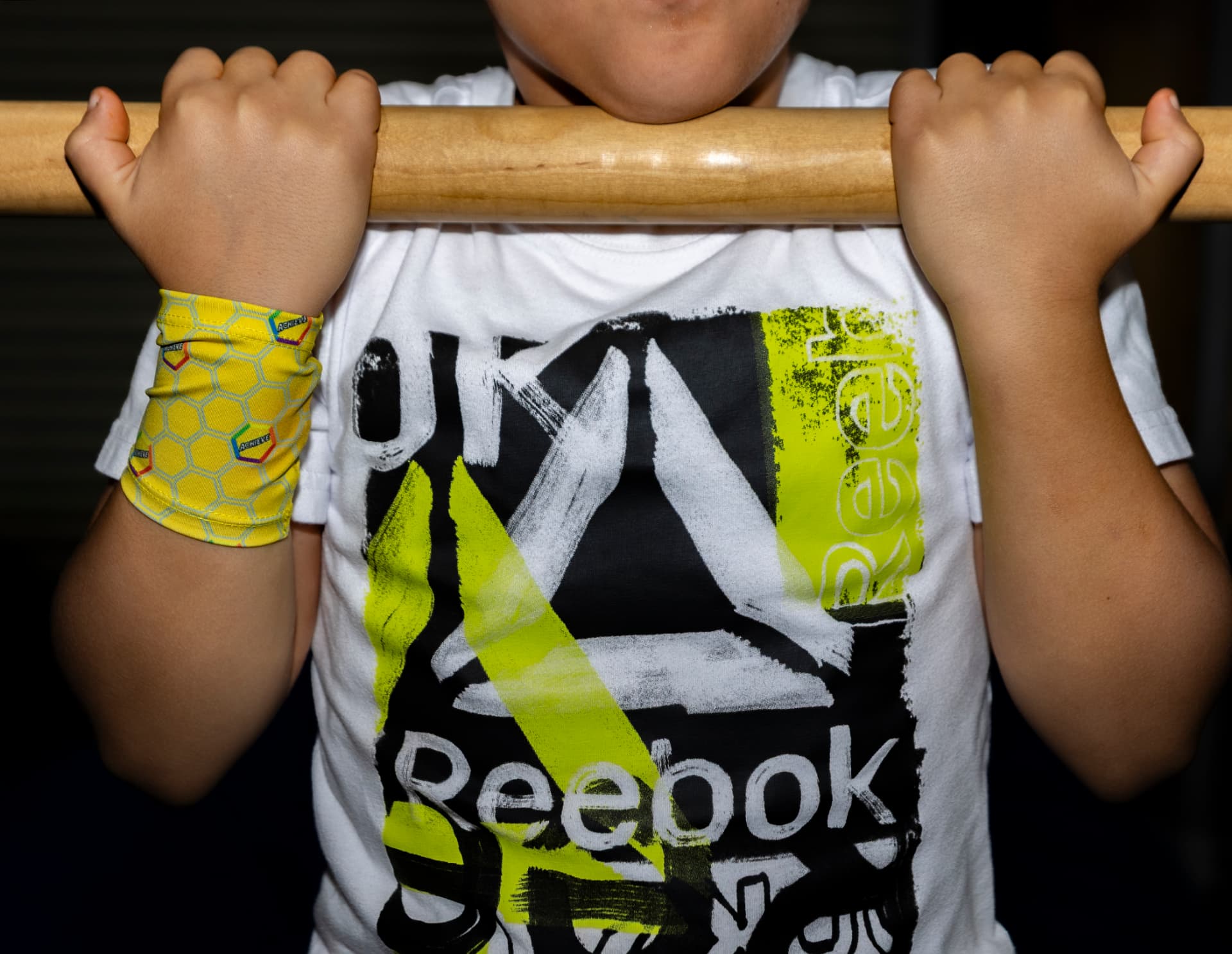 Young ninja gripping the bar wearing an achievement wristband