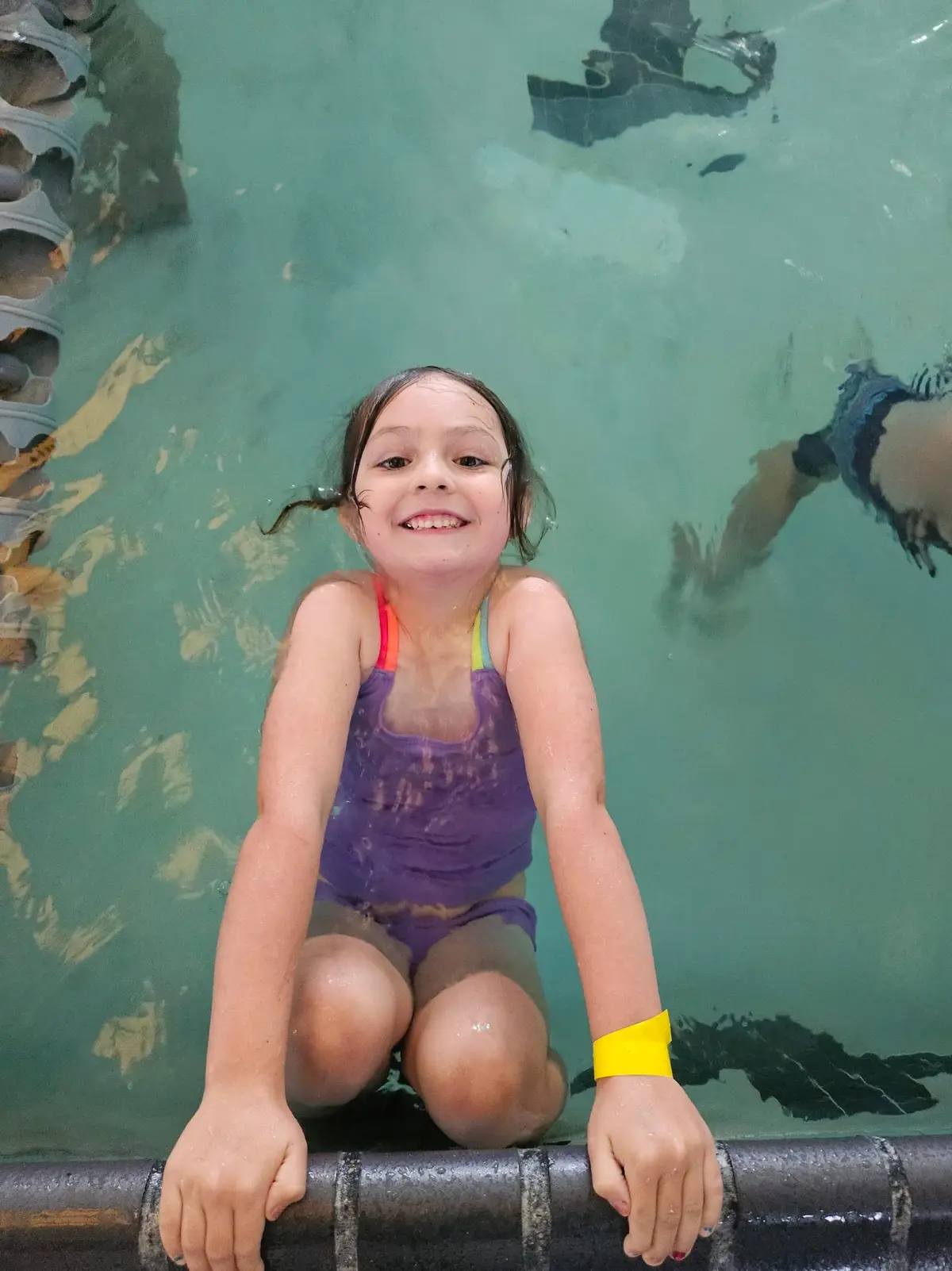 A young swimmer smiling at the wall of the HealthSPORT Arcata pool