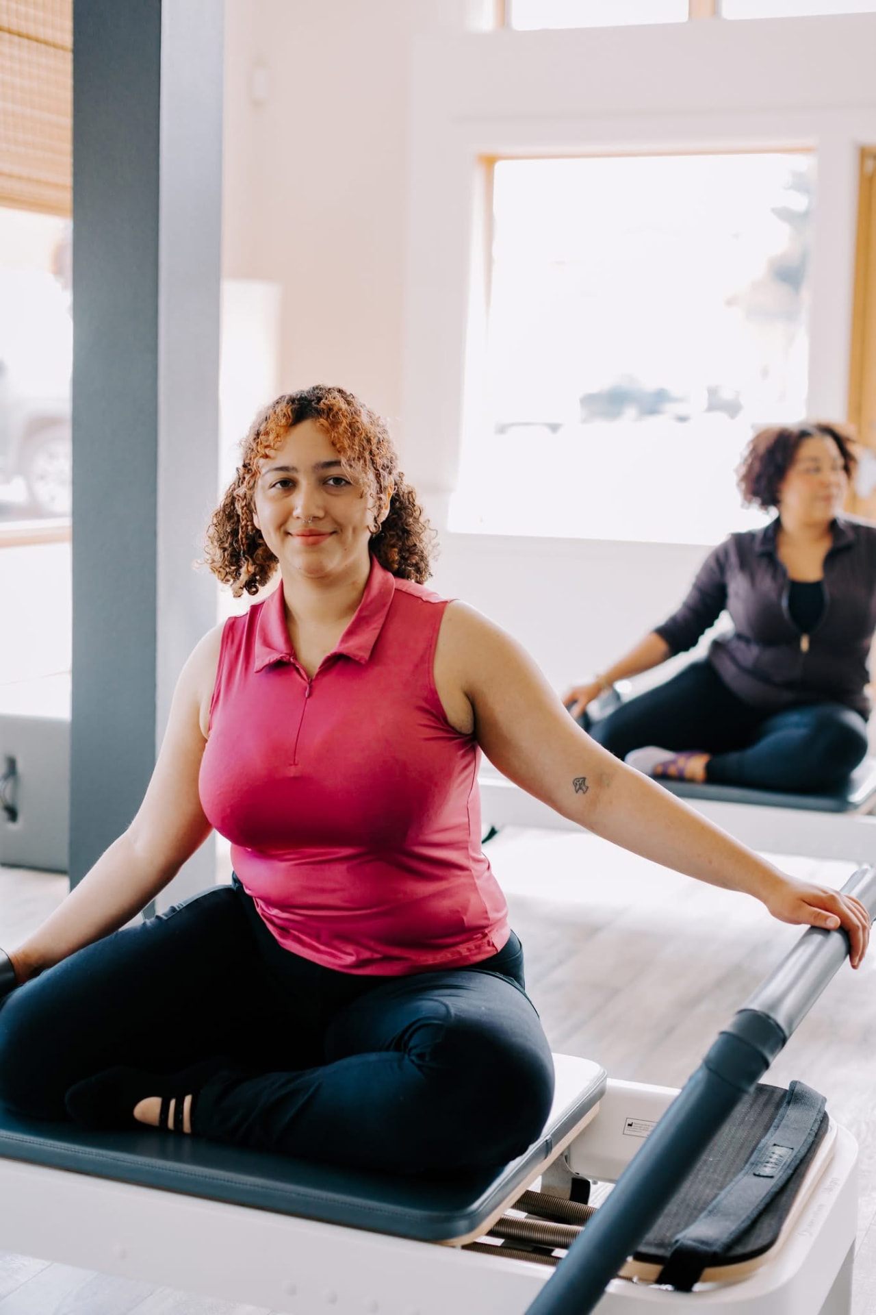 A student seated on a Pilates Reformer smiling during a small-group class