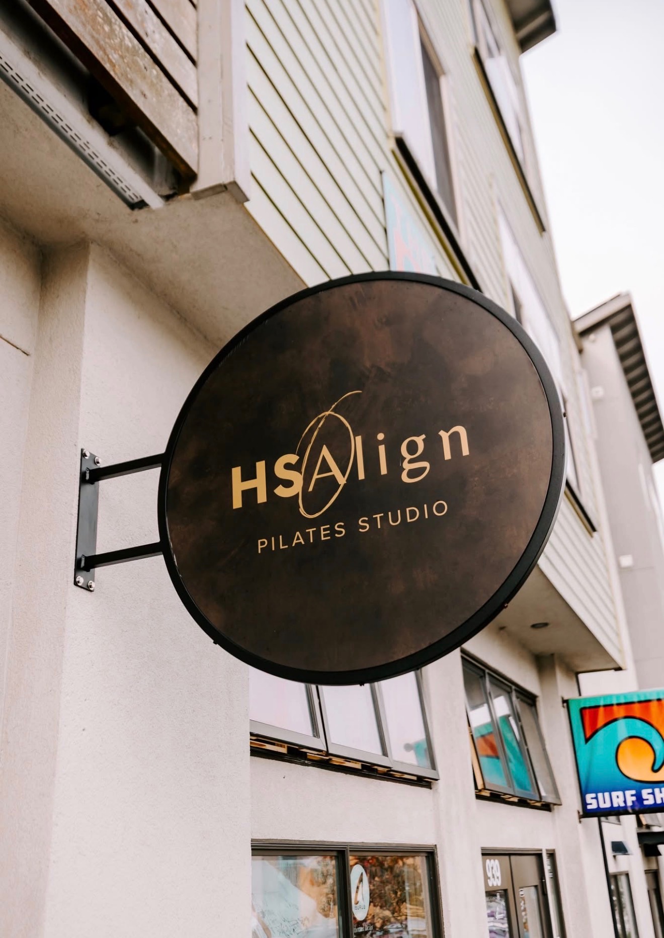 The round black and gold HS Align Pilates Studio sign mounted outside the 8th Street entrance