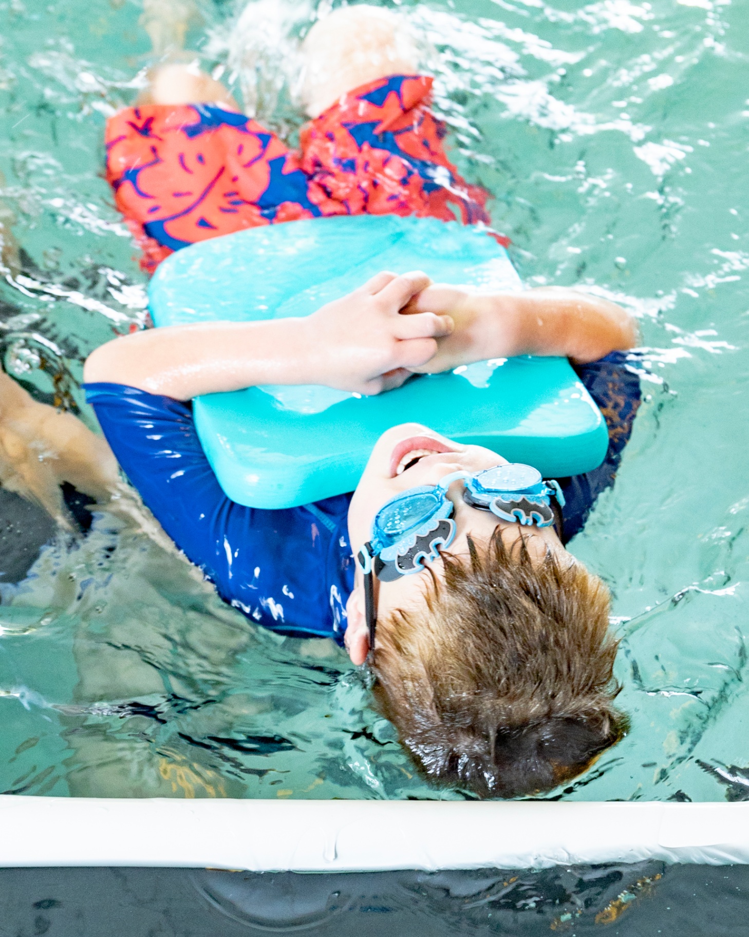 Young swimmer floating on back with kickboard