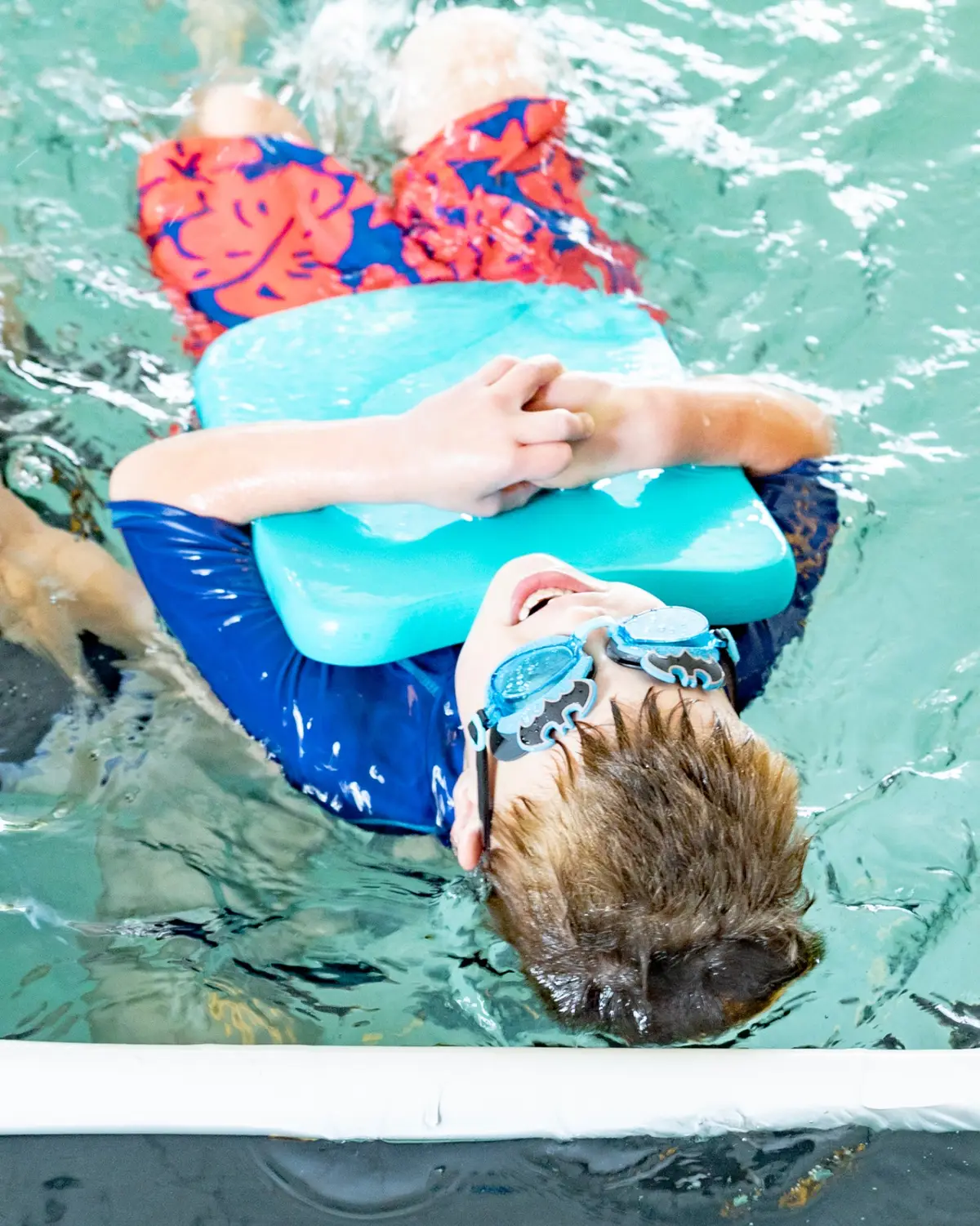 Young swimmer floating on back with kickboard