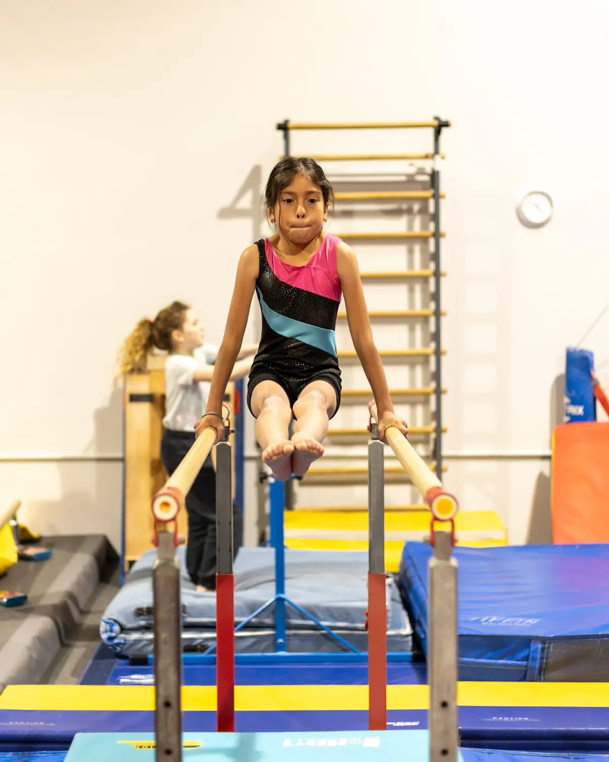 Two gymnasts smiling while hanging from the bars