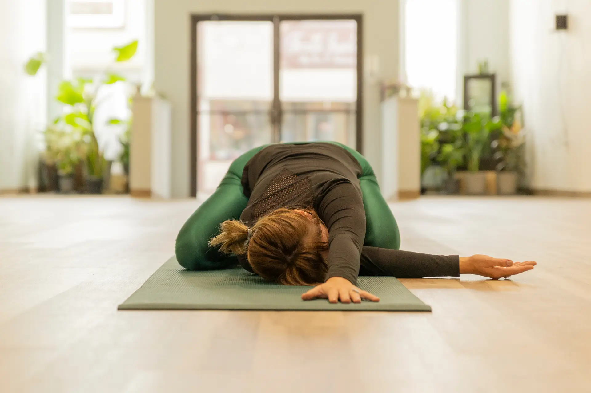 Student resting in child's pose on a green mat in a plant-filled studio
